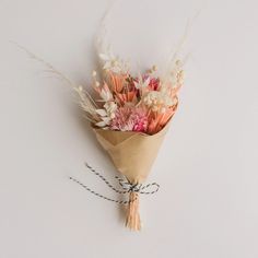 a bouquet of flowers is tied to a white wall with some twine on it