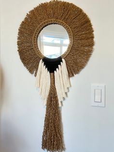 a round mirror with tassels hanging from it's sides on a wall