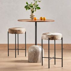 two stools and a table with fruit on it in front of a white wall