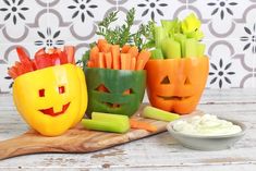 three carved pumpkins, carrots and celery sticks on a cutting board