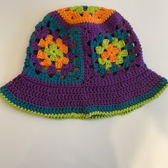 a crocheted purple and green hat with flowers on the front, sitting on a white surface