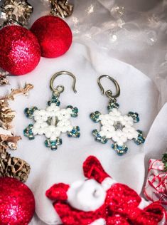 two pairs of earrings sitting on top of a white cloth next to christmas ornaments and baubles