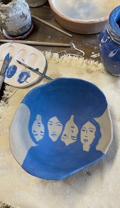 a bowl with the faces of three women painted on it next to paintbrushes