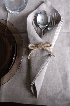 a place setting with silverware and napkins on a linen tablecloth, along with a glass plate