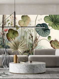 a living room with large green leaves on the wall and a marble coffee table in front of it