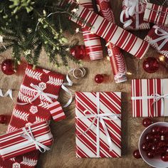 christmas presents wrapped in red and white paper on a wooden table next to a tree