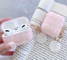 a person holding an airpods in their hand next to a book with ear buds on it