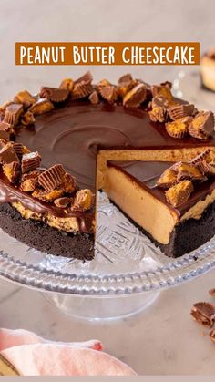 a chocolate peanut butter cheesecake on a glass cake plate with one slice cut out