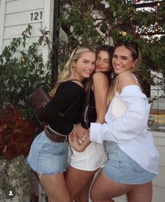 three beautiful young women standing next to each other in front of a white house with trees