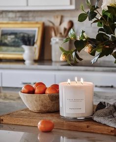 a white candle sitting on top of a table next to some oranges in a bowl