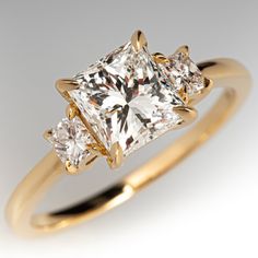 This graceful three-stone engagement ring is centered with one (1) princess cut diamond, weighing 1.51 carats, set into a four-prong claw setting. The center diamond is accented to each side by one (1) princess cut diamond set into a four-prong claw setting. The ring measures 7.2mm at the top, rises 5.3mm above the finger, tapering to 1.5mm wide and 1.3mm thick at the base of the shank. It is currently a size 6.5. Three Stone Princess Cut Ring, 3 Stone Princess Cut Ring, Gold Princess Cut Engagement Ring, Princess Cut Engagement Ring, Princess Cut Engagement Rings Gold, Antique Engagement Rings Sapphire, Engagement Rings Wedding Bands Set, Gold Band Wedding Ring, Princess Diamond Engagement Rings