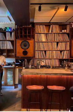 a man standing in front of a bar with lots of records on the walls and shelves