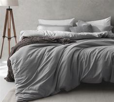 a bed with grey sheets and pillows in a room