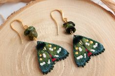 a pair of green and white butterfly earrings on top of a wooden slice with beads