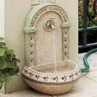 a water fountain sitting on the side of a building next to a potted plant