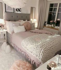 a white and pink bedroom with lights on the windowsills, a large bed covered in blankets and pillows