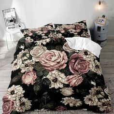 a bed covered in black and pink flowers on top of a wooden floor next to a night stand