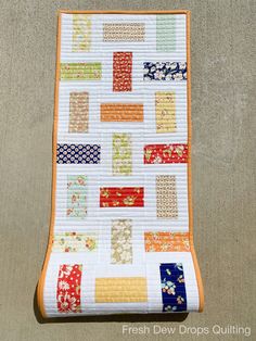 an orange and white quilted table runner with colorful strips on the edge, sitting on top of a gray surface