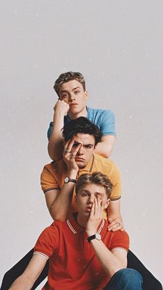 three men sitting on top of each other posing for the camera with their hands to their face