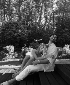 black and white photograph of two people sitting on a wooden deck with trees in the background