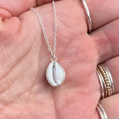 This beautiful necklace features an ethically sourced native cowrie shell in a custom made solid recycled silver wrapped setting with a silver chain.  Every necklace is handmade to order with the silver setting made custom for each shell, making each one unique.  This style 'wraps' the silver only around the edge of the shell holding it securely, whilst showing off both sides of the shell. There are two types of cowrie shell native to Cornwall, the European Cowrie ( Trivia monarcha ) and the Northern Cowrie ( Trivia arctica ).  The European cowrie is easily distinguishable from the Northern by the 3 dark spots on its shell and the fact it can grow to a larger size. I find many cowries whilst beach-combing in Cornwall and they are one of the small number of shells I use in my jewellery. Wit Silver Shell Necklace For Gifts, Silver Shell Necklace As A Gift, Silver Shell Necklace For Gift, Silver Shell Necklace Perfect For Gifts, White Shell Charm Necklace Gift, Unique White Shell Pendant Necklace, Unique White Pendant Shell Necklace, Handmade Silver Shell Pendant, Silver Shell Pendant Jewelry