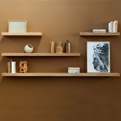 three wooden shelves with books, vases and other items on them against a brown wall