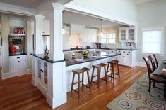 a kitchen with white cabinets and black counter tops, wooden flooring and an island in the middle