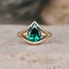 a gold ring with an emerald colored stone in the center on top of a rock