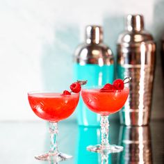 two cocktails with raspberries sit on a table