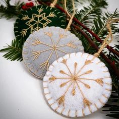 three ornaments are hanging from a christmas tree branch with evergreen needles and snowflakes