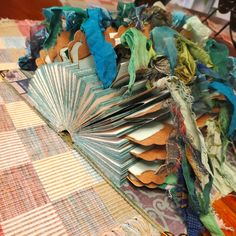 an open book sitting on top of a table covered in colorful papers and cloths