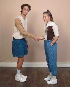 a man and woman standing next to each other in front of a wall holding hands