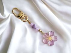 a pink flower is attached to a gold keychain on a white satin background