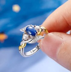 a person holding a ring with blue and white stones on it's side, in front of a blue background