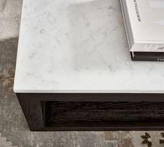 a book sitting on top of a white marble topped coffee table next to a rug