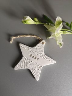 a ceramic star ornament hanging from a string with flowers in the corner on a gray surface