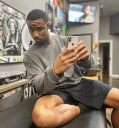 a man sitting in a barber shop looking at his cell phone while he sits on the chair