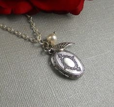 "This Vintage inspired necklace is 28\" long. Small oval silver finished locket with Victorian patterns engraved on the sides is decorated with antique finished tiny silver wing and white swarovski pearl. Pendant locket is finished with silver chain and silver lobster clasp. Locket is almost 23mm in size and opens side ways. It has room for two photos! Thanks for looking:) ~Mani" Sterling Silver Locket Necklace For Vintage Collection, Silver Oval Jewelry For Vintage Collection, Antique Silver Jewelry With Vintage Charm As Gift, Silver Oval Pendant Locket Necklace With Charms, Silver Sterling Silver Locket Necklace With Charms, Silver Locket Necklace With Charms And Oval Pendant, Vintage White Gold Locket Necklace For Gift, Vintage White Gold Locket Necklace As A Gift, Silver Oval Necklaces With Charms