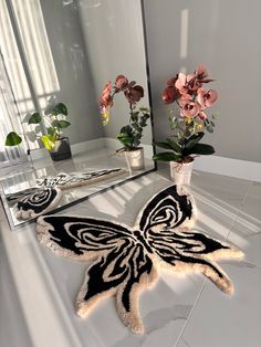 a white table topped with a black and white butterfly rug next to a large mirror