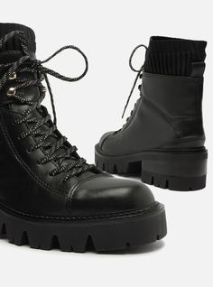 Black leather combat boot. The style features a mid-shaft, a rounded toe and a low rubber heel with a rugged, chunky lug sole with a stacked detailing. It has a snug-fitting vamp, lace closure in the color of the boot and a pull-tab on the back, making it easy to put on. The upper part of the shaft is made of knit material. Why follow this trend?These combat boots are essential items for the season! They feature a chunky lug sole in a super versatile tone and are a guarantee of comfort and style Black Leather Combat Boots, Genuine Leather Boots, Combat Boot, Rounded Toe Boots, Rubber Heels, Lug Sole, Knitting Materials, Lace Closure, Leather And Lace