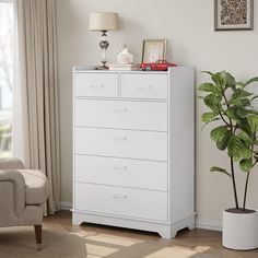 a white chest of drawers in a living room with a chair and potted plant