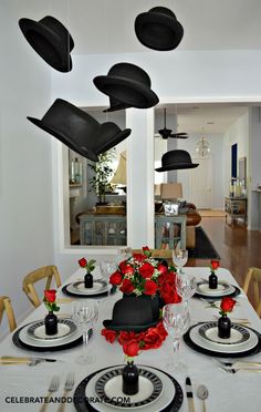 a dining room table is set with black and white plates, silverware, and red roses