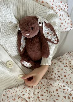 a person is holding a stuffed animal in their hand while laying in bed with the covers pulled down