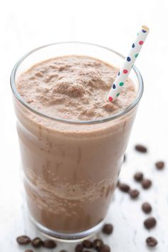 a smoothie in a glass with a straw on the top and coffee beans around it