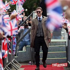 a man in a suit and tie walking down a red carpeted area with british flags