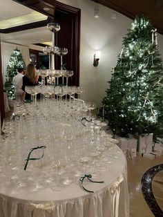 a large table with many wine glasses on it and a christmas tree in the background