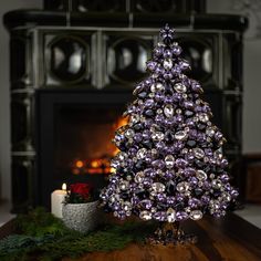 a purple christmas tree sitting on top of a wooden table next to a fire place