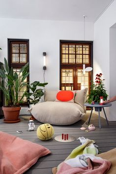 a living room filled with lots of furniture and plants on the floor next to windows