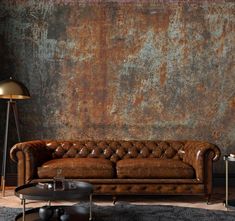 a brown leather couch sitting in front of a rusted wall with a lamp on it