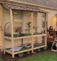 a woman sitting on a porch next to a house with a cat in the window